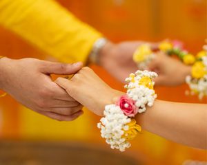 Hands wearing delicate white and pink floral bracelets against a warm orange and yellow background.