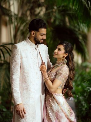 A romantic couple in white and pink wedding attire share an intimate moment in a tropical garden setting.