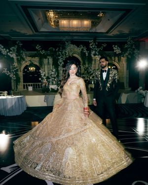 Elegant gold and cream lehenga with intricate embroidery twirls on a dark dance floor at a formal reception.