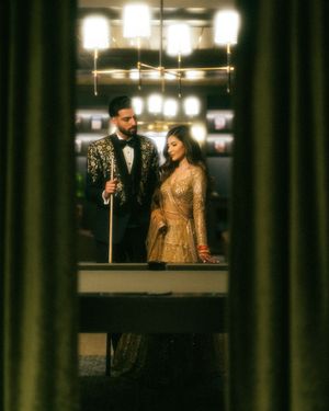 A couple in elegant evening attire shares an intimate moment under warm lighting in a dimly lit space.