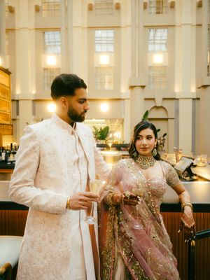 A couple in traditional Indian wedding attire share a moment in an elegant indoor venue with warm lighting.