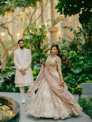 A couple in elegant wedding attire poses in a lush garden setting with soft lighting and greenery in the background.