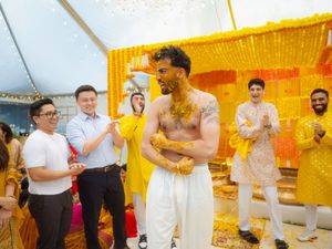 A festive wedding celebration with guests dancing and embracing in a vibrant yellow-decorated venue.