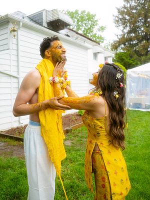 Two people covered in bright yellow powder laugh and celebrate together against a white house backdrop.