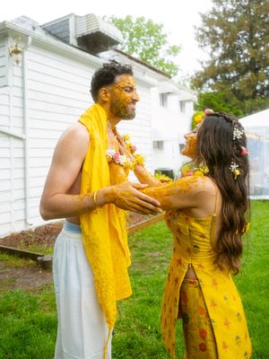 Couple wearing yellow traditional Indian outfits covered in turmeric powder celebrate during a pre-wedding Haldi ceremony.