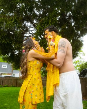 A couple in yellow floral robes and white dress embrace and dance playfully in a backyard garden setting.