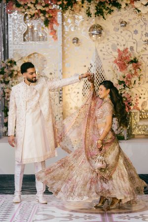 A couple in traditional South Asian wedding attire dancing and twirling in an elegant venue with floral decor.