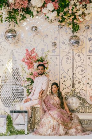 Elegant wedding decor with pink and white floral arrangements against an ornate lattice backdrop with hanging disco balls.