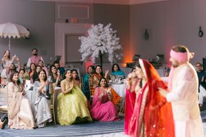 A group of people in vibrant traditional dresses and gowns gathered at a formal indoor celebration.