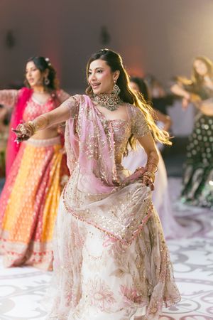 A group performs traditional Indian dance moves in colorful lehengas at a wedding reception celebration.