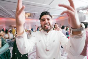 Guests in traditional white kurtas dance joyfully at an Indian wedding celebration.
