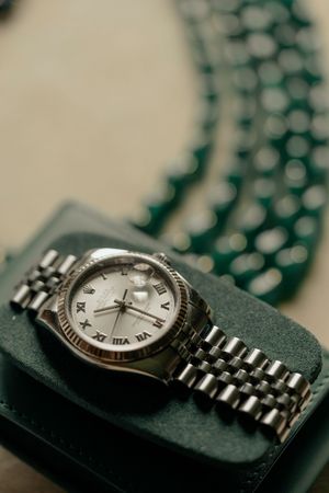 A silver luxury watch with Roman numerals on a green display cushion, showcasing elegant metallic bracelet details.