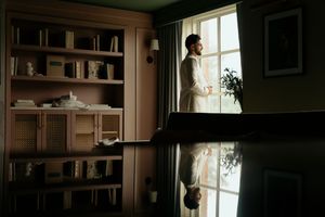 A dark, moody interior room with bookshelves and window light creating dramatic shadows and silhouettes.