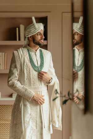 Traditional white Indian sherwani with intricate embroidery and turquoise necklace shown in multiple angles.