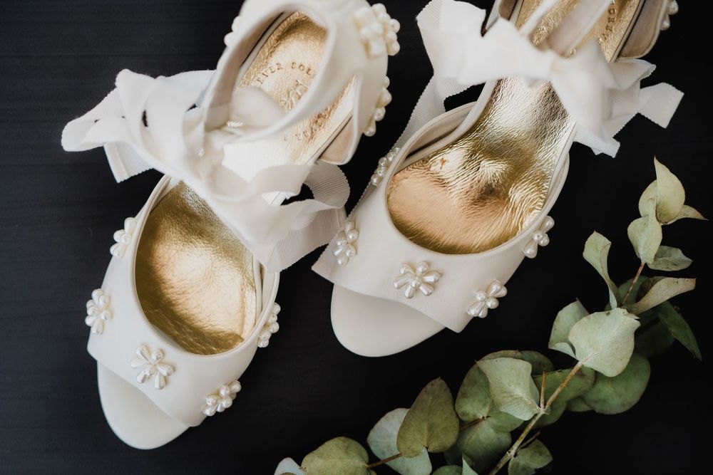 Elegant white bridal shoes with delicate details displayed against a dark background.