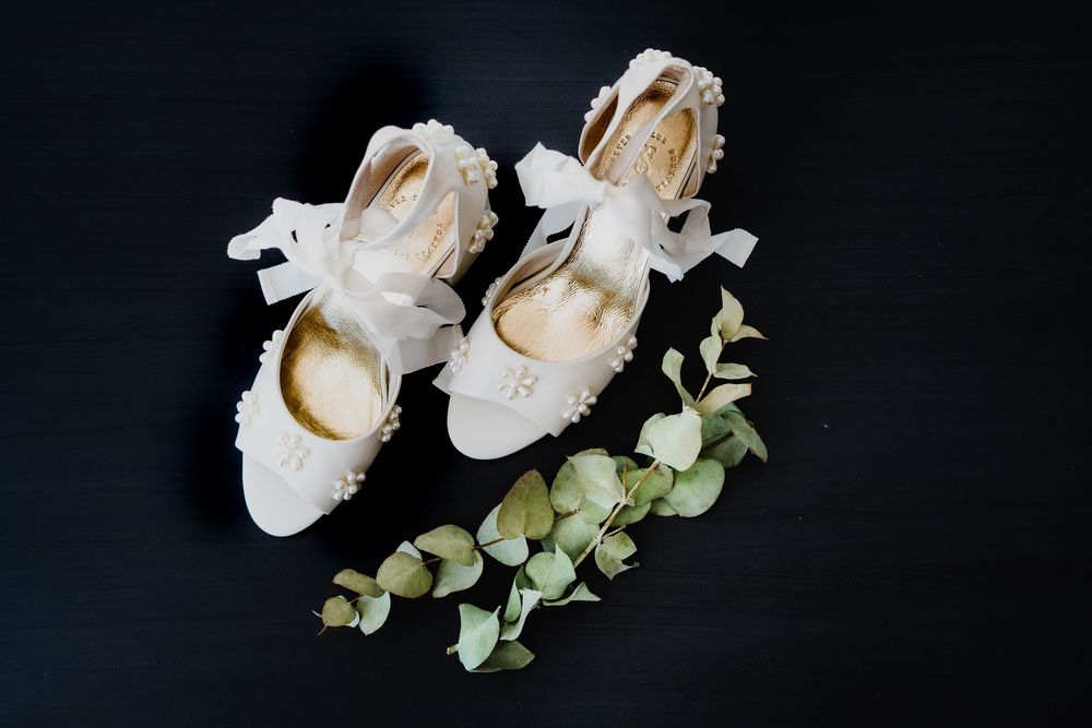 White wedding shoes arranged with eucalyptus leaves on black background.