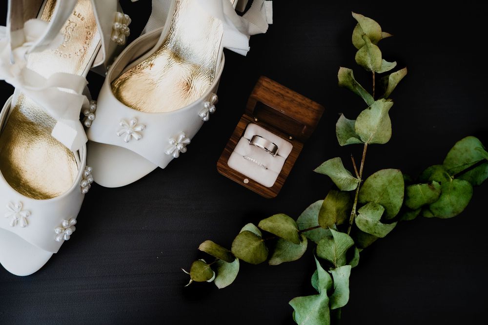 Wedding accessories including white shoes and floral elements arranged on dark background.