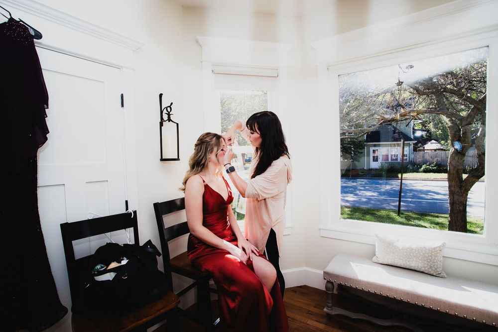 Wedding preparation scene in a bright white room with natural light streaming through windows.