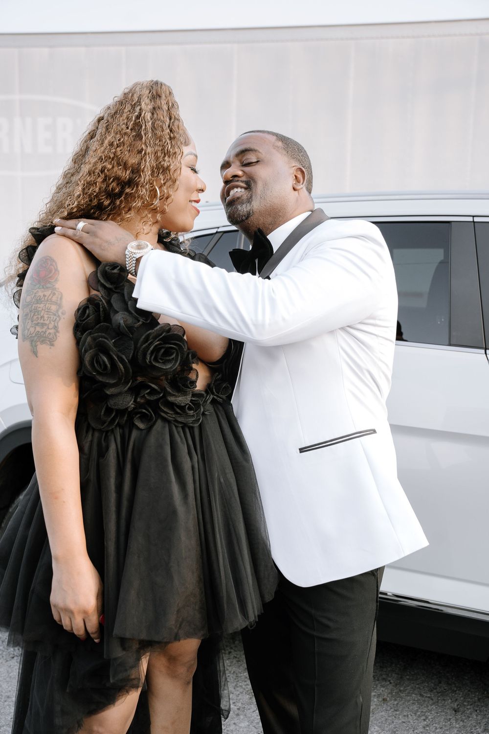 Romantic couple in black dress and white shirt share intimate moments in an outdoor photoshoot.