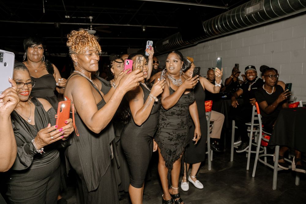 People dancing and socializing at a dimly lit party venue with phones raised in celebration.
