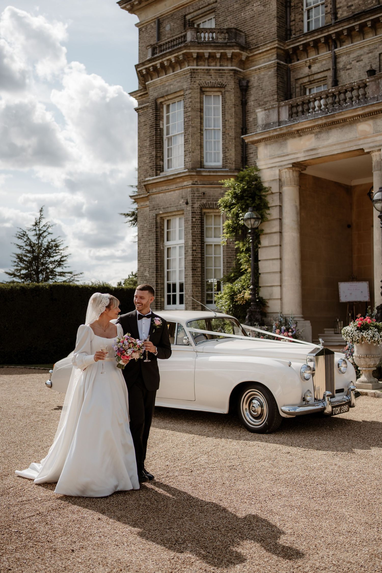 A wedding couple sharing a kiss outside Hedsor House with floral decorations.