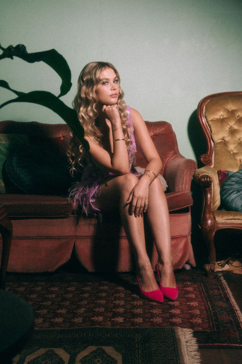 Vintage-inspired portrait of model in purple dress seated on brown velvet sofa with decorative lamp.