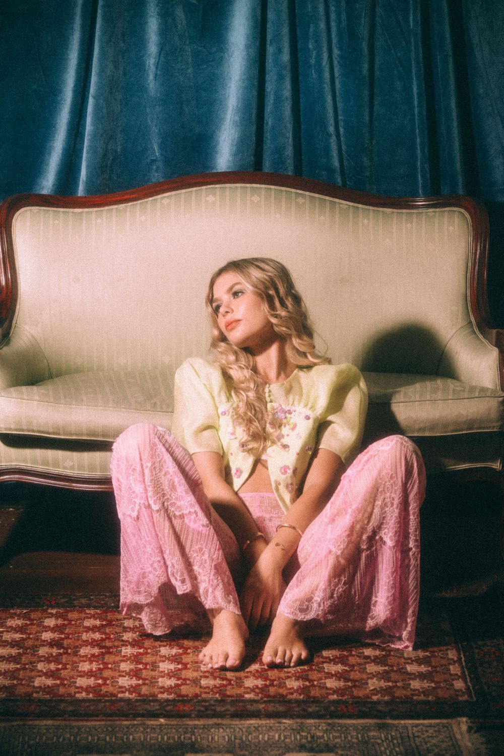 Casual portrait on vintage sofa featuring pink lace pants and cream colored top.
