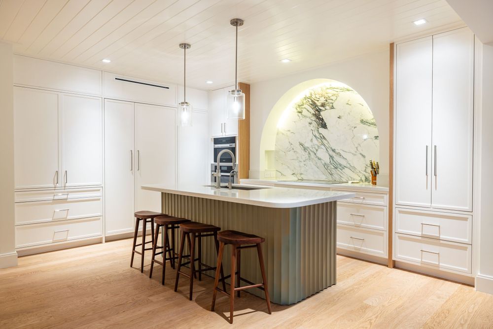 Modern white kitchen with marble accent wall, wooden island, and pendant lighting over bar seating.