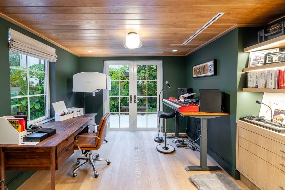 Home office with dark green walls, wooden desk, and French doors leading to outdoor space.