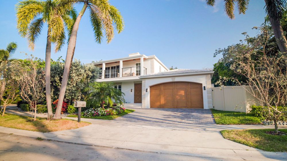 Modern white mansion with palm trees and curved driveway in affluent Miami neighborhood.