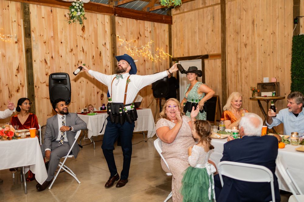 A reception celebration in a rustic wooden barn venue with guests seated at tables while someone dances in the center.