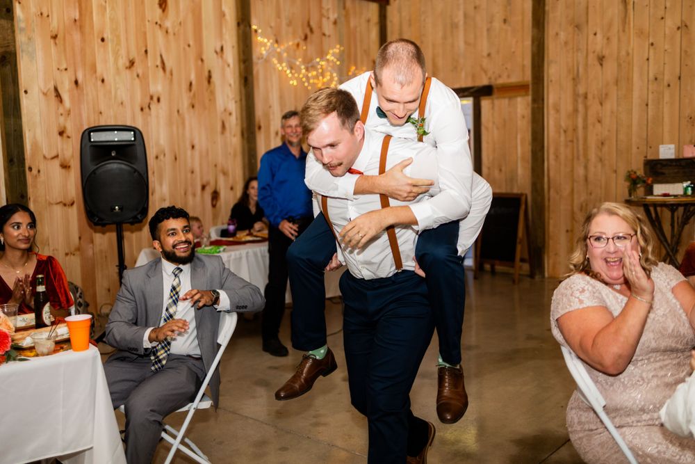 Wedding guests laugh and dance during an energetic reception celebration inside a rustic wooden barn venue.