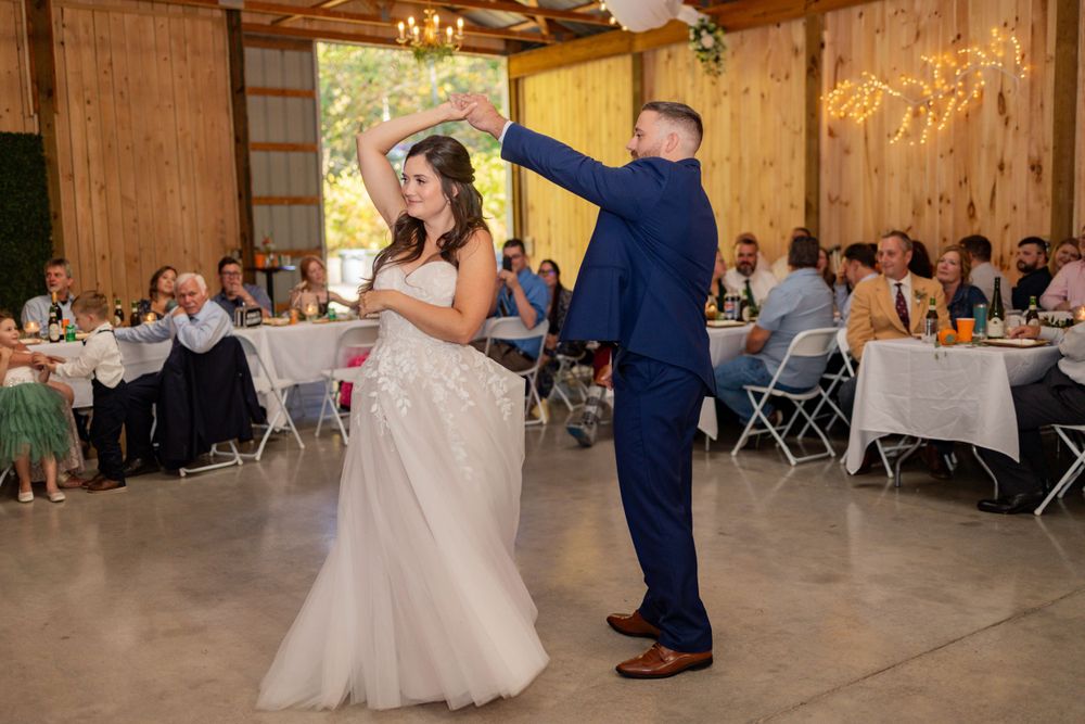 A couple dances together during their wedding reception in a rustic wood-paneled venue with guests seated at tables.