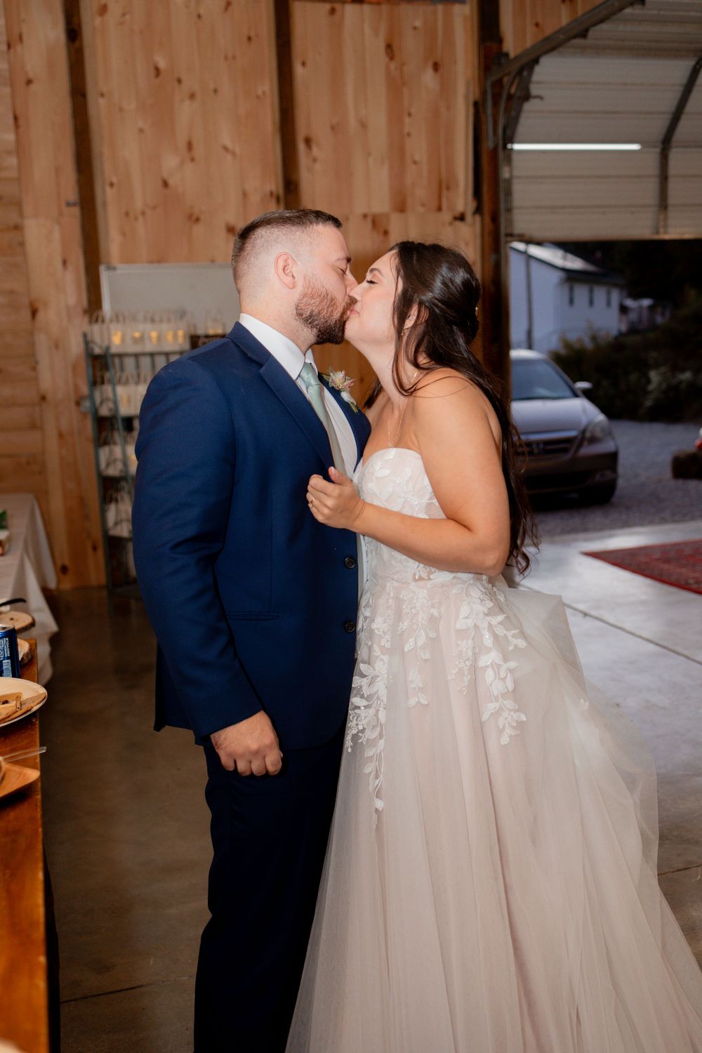A romantic moment between newlyweds sharing their first kiss in a rustic barn venue setting.