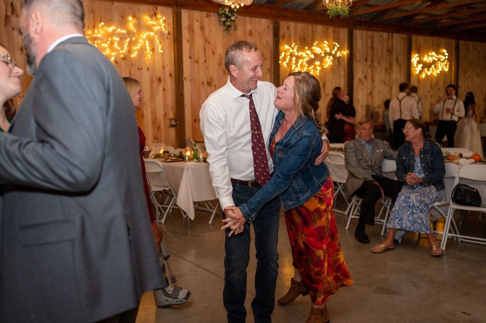 People enjoying a lively dance moment at a rustic barn reception with warm lighting and decorative elements.