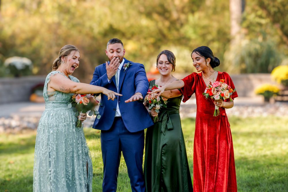 Wedding party members laugh together outdoors while holding floral bouquets in formal attire.