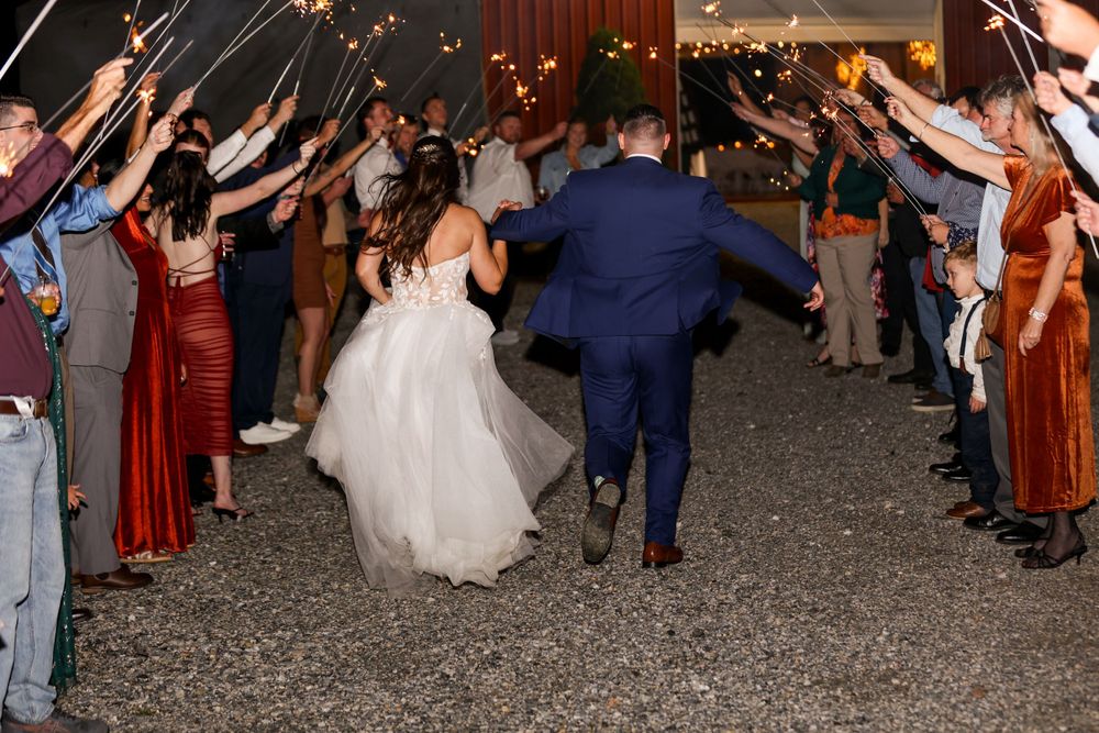 Newlyweds make their grand exit through a sparkler tunnel at outdoor wedding reception while guests cheer.