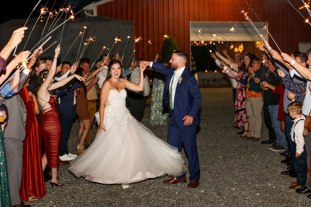 Wedding party guests form a sparkler tunnel exit celebration for couple dancing at rustic barn venue.