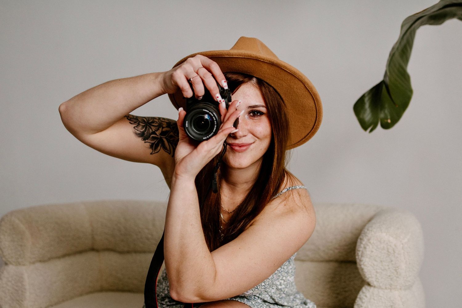 Person in brown hat holding vintage camera while sitting on beige couch.