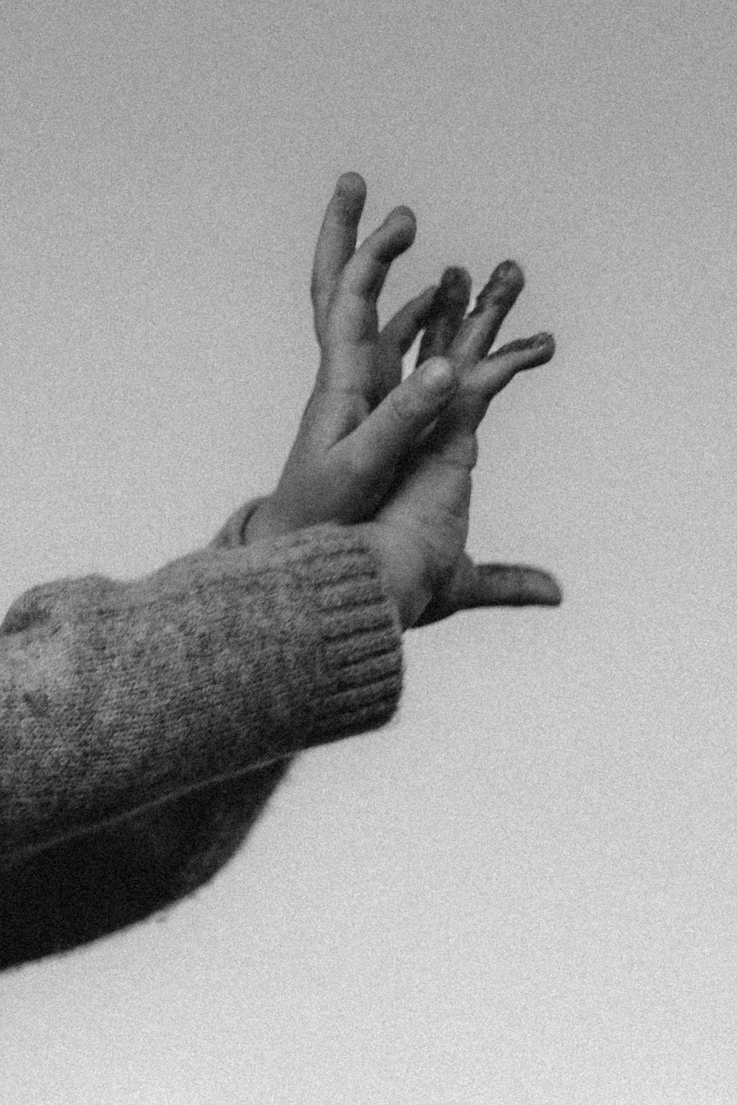 A black and white artistic photograph in Denia of outstretched hands with a knit sweater sleeve reaching upward. Denia photographer