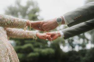 Close-up of couple holding hands with wedding rings and traditional henna designs.