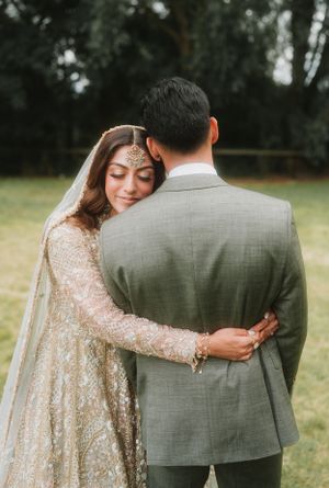 Intimate moment between newlyweds in traditional South Asian wedding attire outdoors.