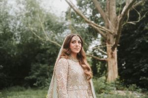 Bride in sparkly champagne lehenga poses in front of trees outdoors.
