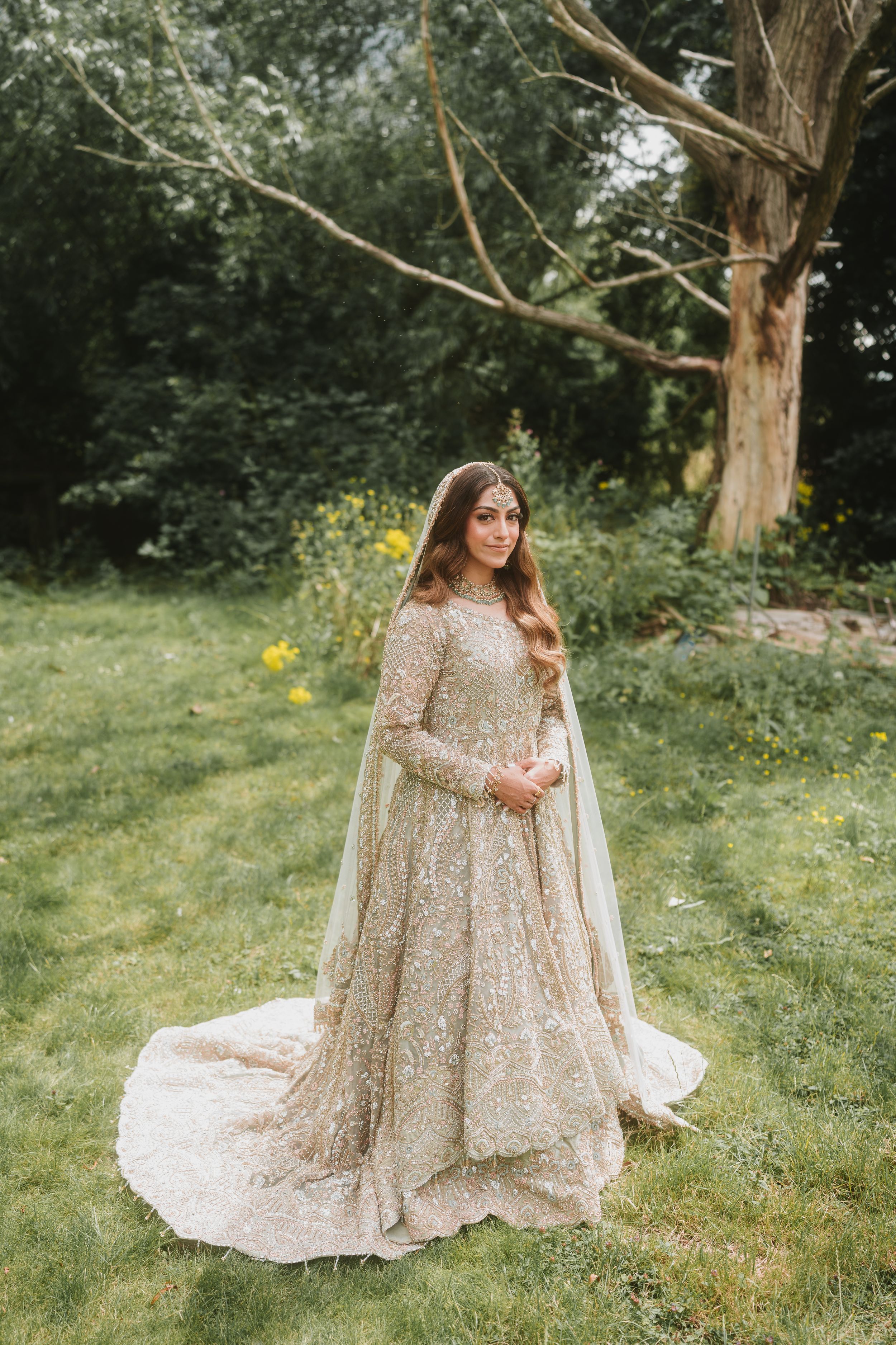 Elegant bride in champagne lehenga poses in outdoor garden setting.