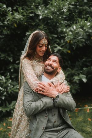 Intimate moment between newlyweds as bride embraces groom from behind in garden setting.