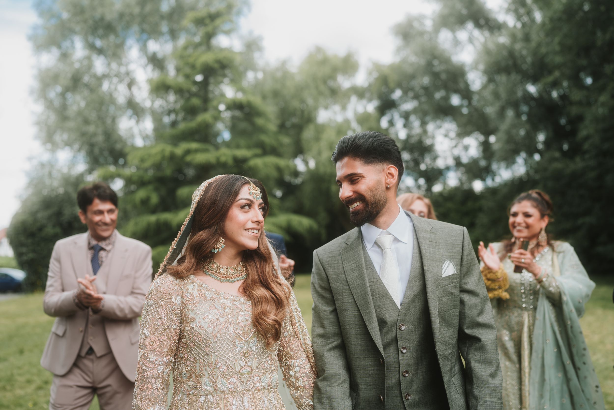 Candid wedding photo showing joyful couple with wedding party celebrating in background.