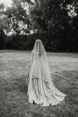 Dramatic black and white photo of bride in flowing lace gown and veil in garden setting.