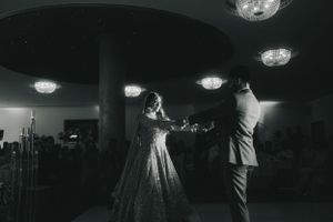 A couple dancing in a ballroom under crystal chandeliers in black and white.