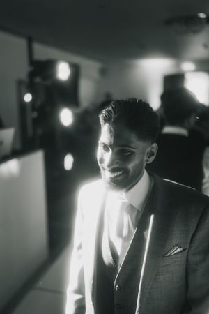 Black and white portrait of a wedding guest smiling in formal attire with dramatic lighting.