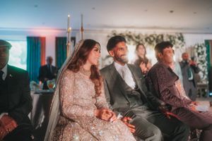 Wedding ceremony guests seated indoors with decorative lighting and floral arrangements.